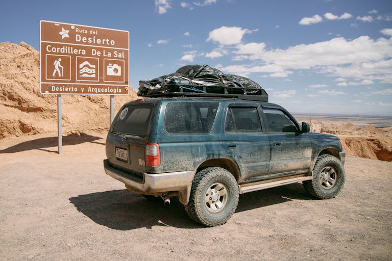 A dusty SUV parked near a sign in Cordillera de la Sal, Chile's Atacama Desert.